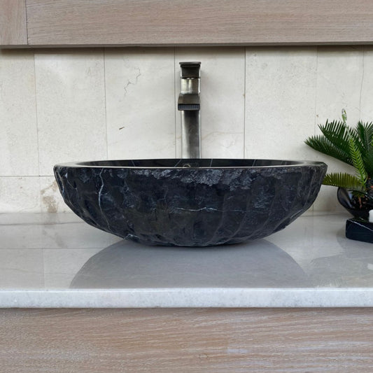 Handcrafted black marble round bowl vessel sink with chiseled exterior, polished interior, and natural white veining displayed on a modern bathroom vanity countertop.
