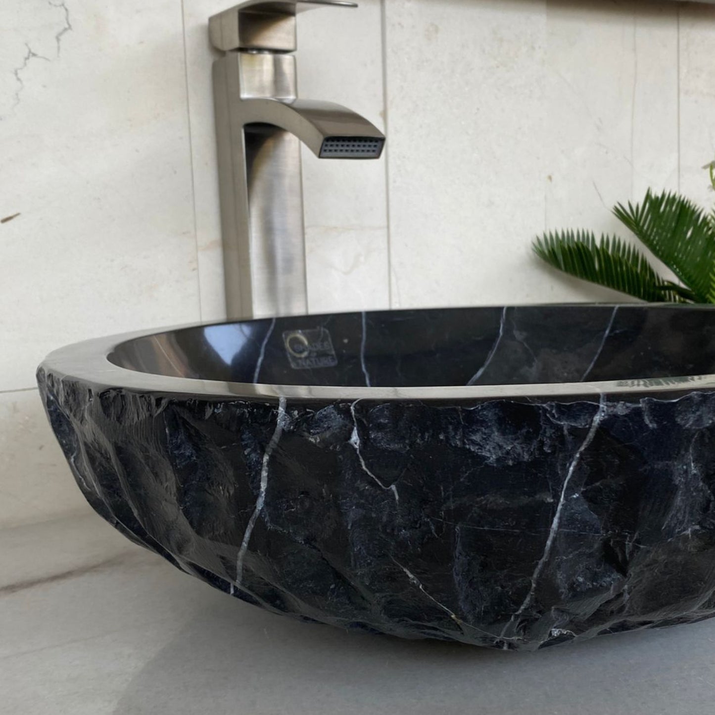 Side profile of handcrafted black marble vessel sink showing polished interior, chiseled natural stone exterior, and distinctive white veining for luxury bathroom vanity installation.