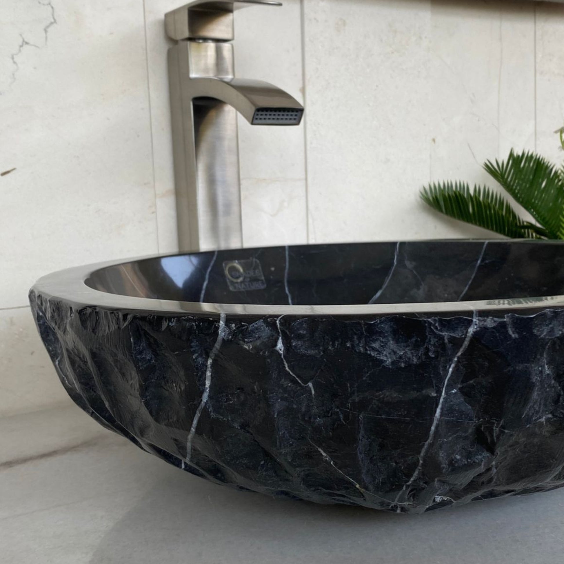 Side profile of handcrafted black marble vessel sink showing polished interior, chiseled natural stone exterior, and distinctive white veining for luxury bathroom vanity installation.