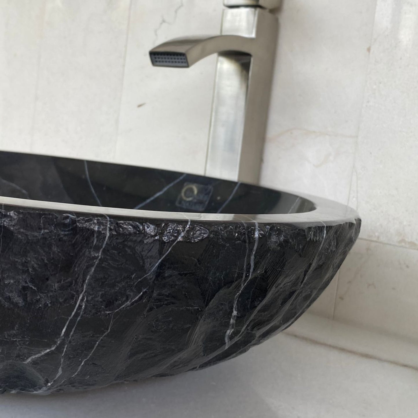 Close-up of handcrafted black marble vessel sink featuring polished interior edge, chiseled natural stone exterior texture, and distinctive white marble veining for luxury bathroom design.