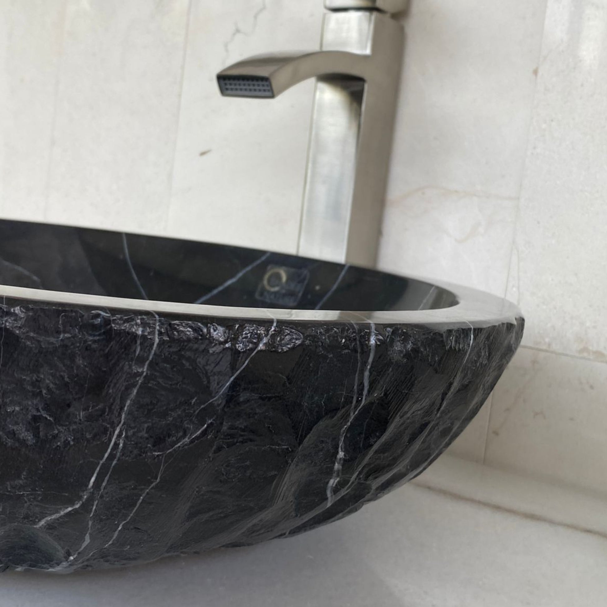 Close-up of handcrafted black marble vessel sink featuring polished interior edge, chiseled natural stone exterior texture, and distinctive white marble veining for luxury bathroom design.