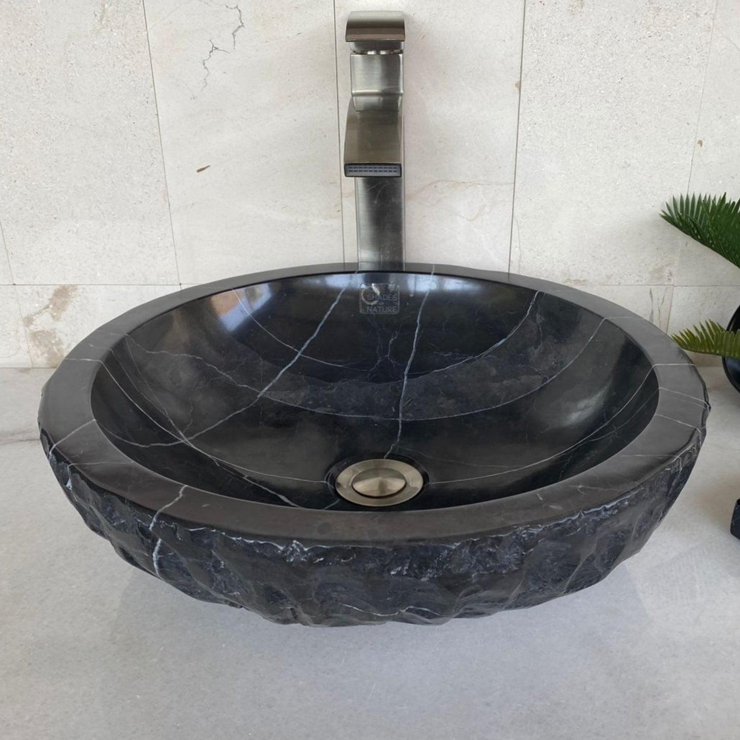 Front angle view of handcrafted black marble round bowl vessel sink with polished interior, chiseled natural stone exterior, and white marble veining for modern luxury bathroom vanity installation.