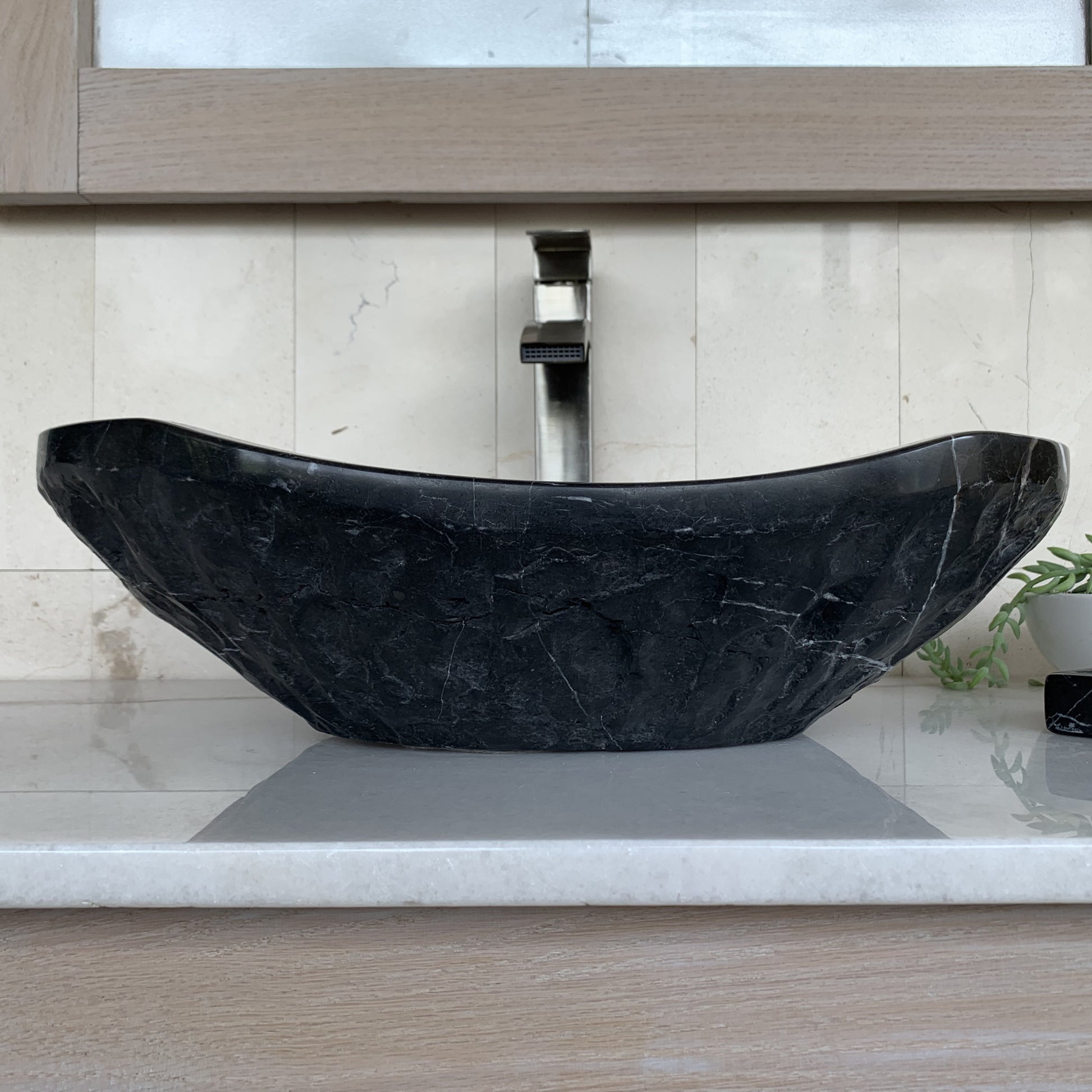 Handcrafted black marble oval vessel sink featuring sculpted chiseled natural stone exterior, elegant curved silhouette, natural white marble veining, and luxury bathroom vanity styling.