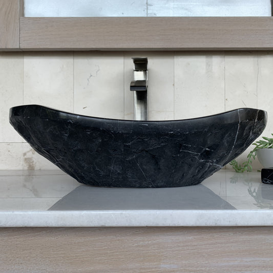 Handcrafted black marble oval vessel sink featuring sculpted chiseled natural stone exterior, elegant curved silhouette, natural white marble veining, and luxury bathroom vanity styling.