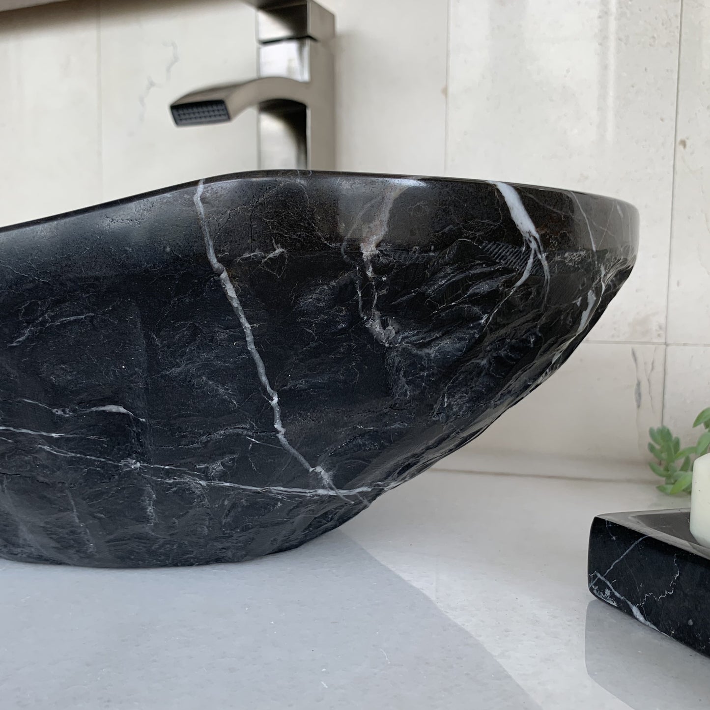 Close-up of handcrafted black marble oval vessel sink showing sculpted chiseled natural stone exterior texture, elegant curved silhouette, natural white marble veining, and luxury bathroom craftsmanship.