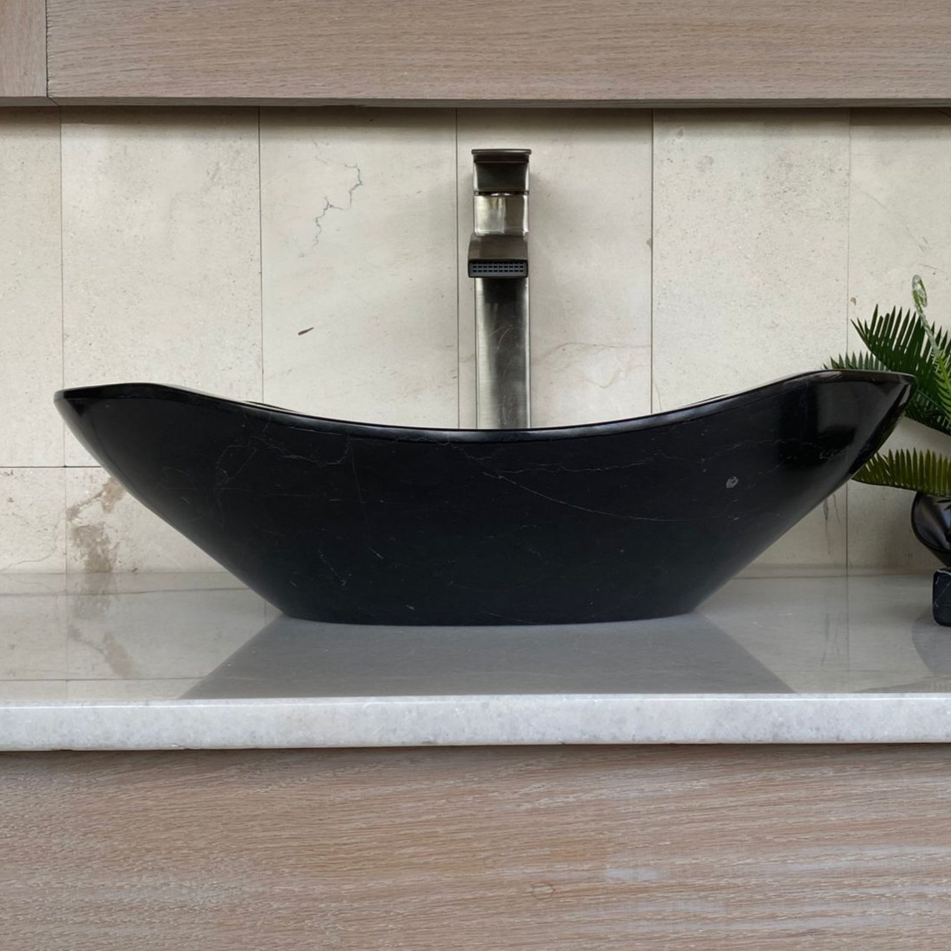 Handcrafted black marble oval vessel sink with polished interior, elegant curved silhouette, natural marble veining, and luxury above-counter bathroom vanity design.