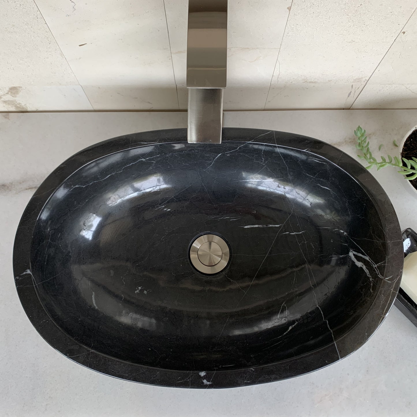 Top view of handcrafted black marble oval vessel sink featuring polished interior basin, natural white marble veining, elegant oval design, and standard center drain for luxury bathroom vanity installation.