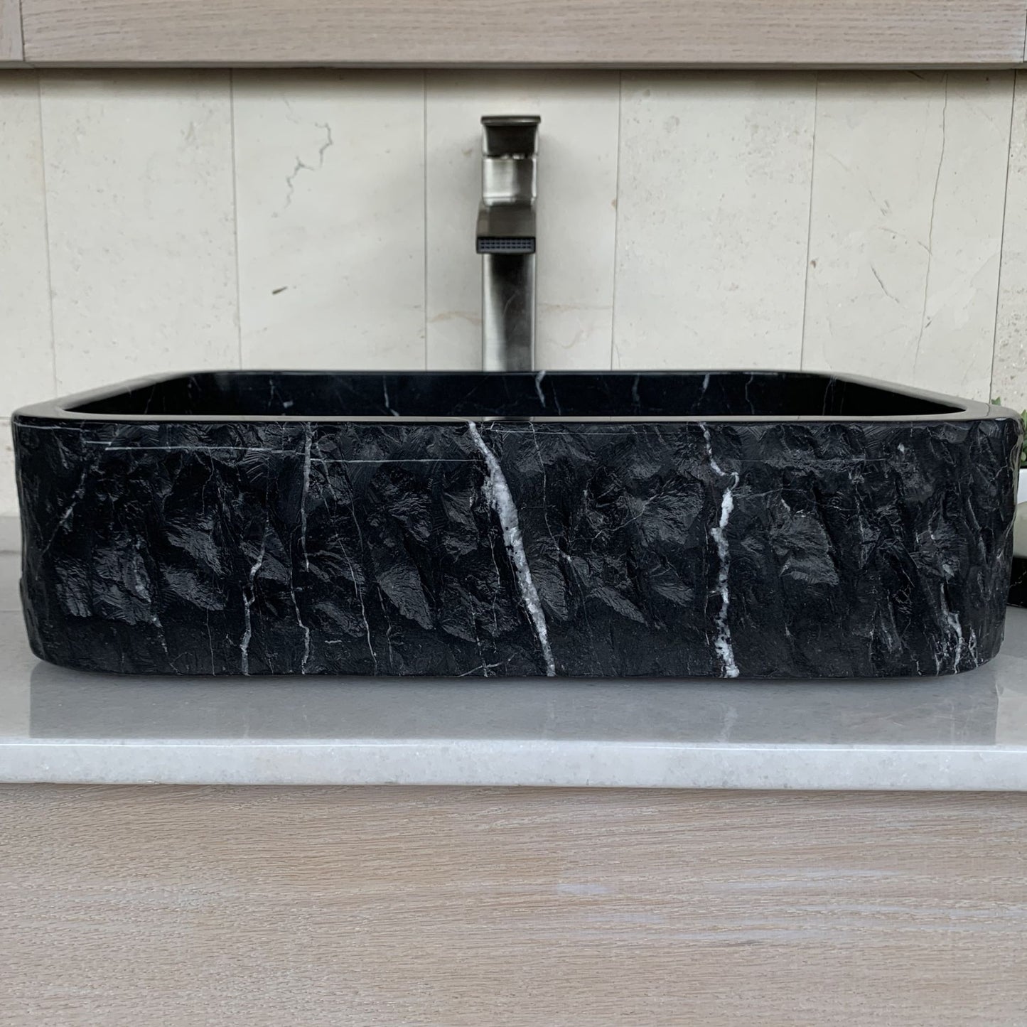 Handcrafted black marble rectangle vessel sink with polished interior, chiseled natural stone exterior, and white marble veining displayed on a modern bathroom vanity countertop.