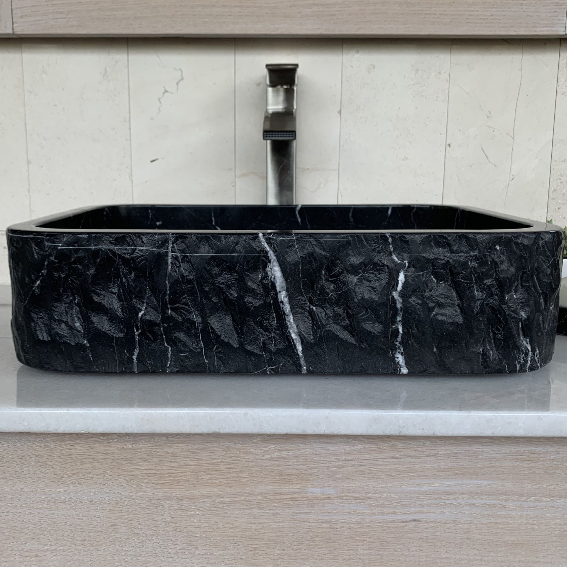 Handcrafted black marble rectangle vessel sink with polished interior, chiseled natural stone exterior, and white marble veining displayed on a modern bathroom vanity countertop.