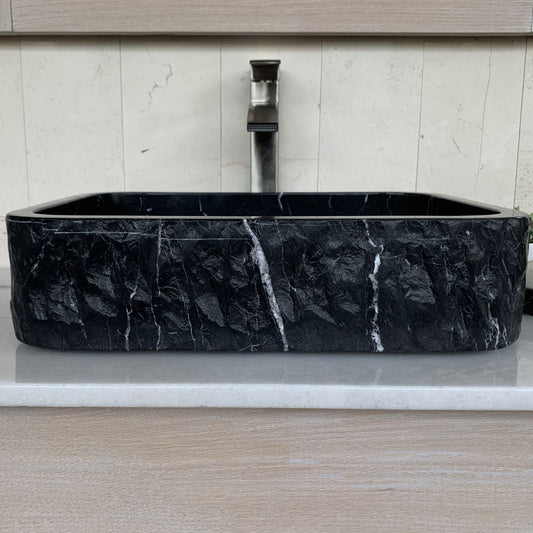 Handcrafted black marble rectangle vessel sink with polished interior, chiseled natural stone exterior, and white marble veining displayed on a modern bathroom vanity countertop.