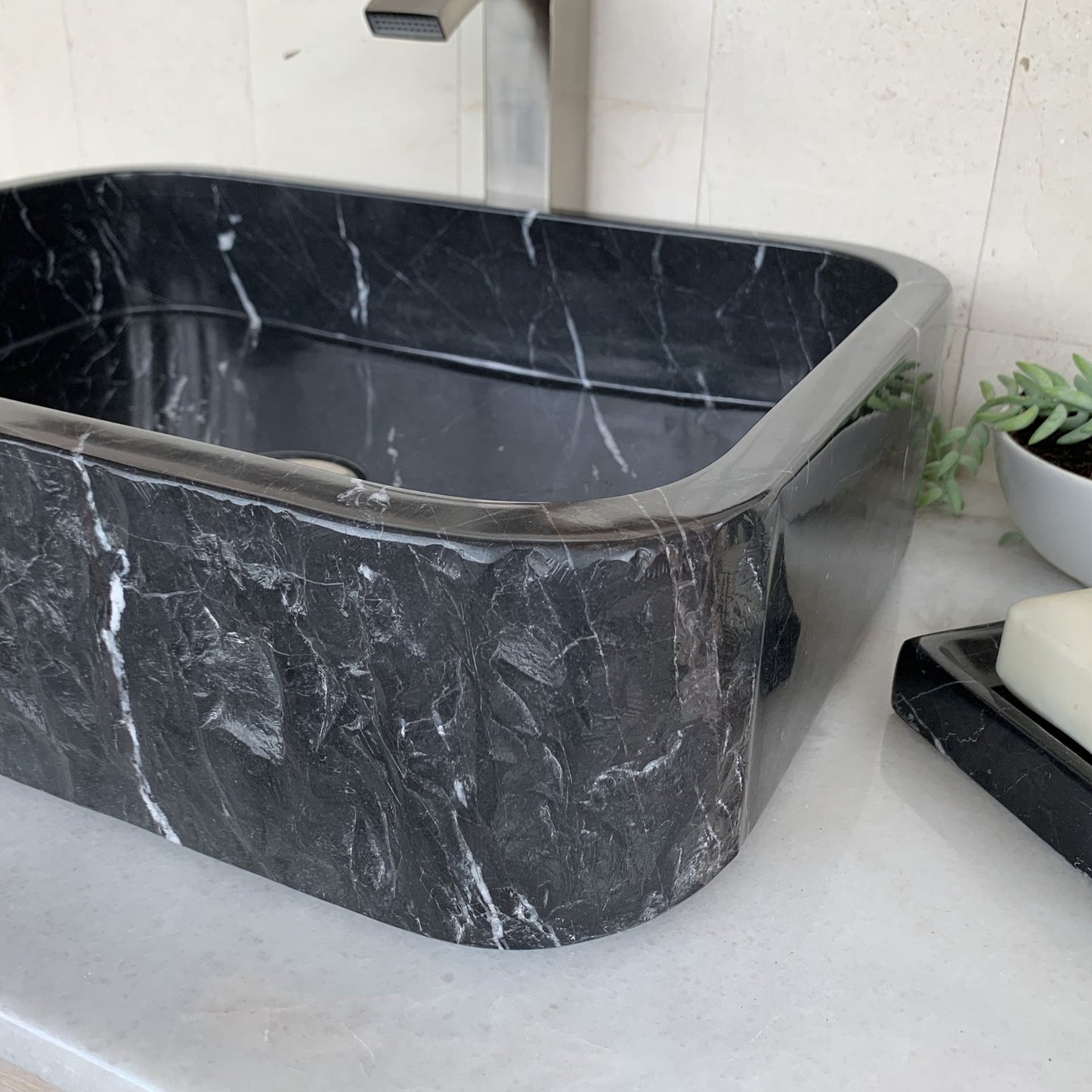 Angled close-up view of handcrafted black marble rectangle vessel sink featuring polished interior, rounded corner rectangular design, natural white marble veining, and luxury bathroom vanity styling.