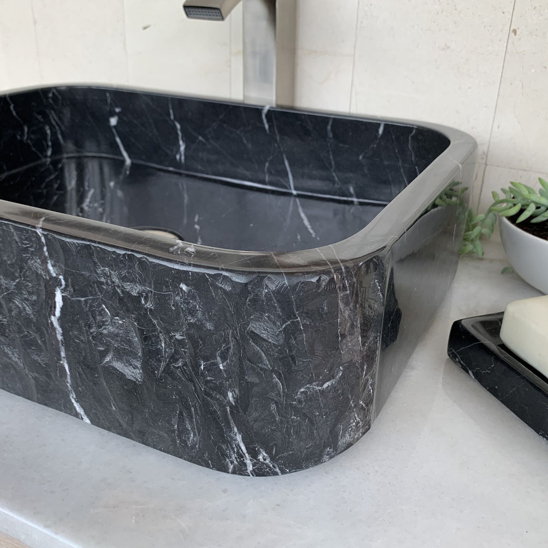 Angled close-up view of handcrafted black marble rectangle vessel sink featuring polished interior, rounded corner rectangular design, natural white marble veining, and luxury bathroom vanity styling.