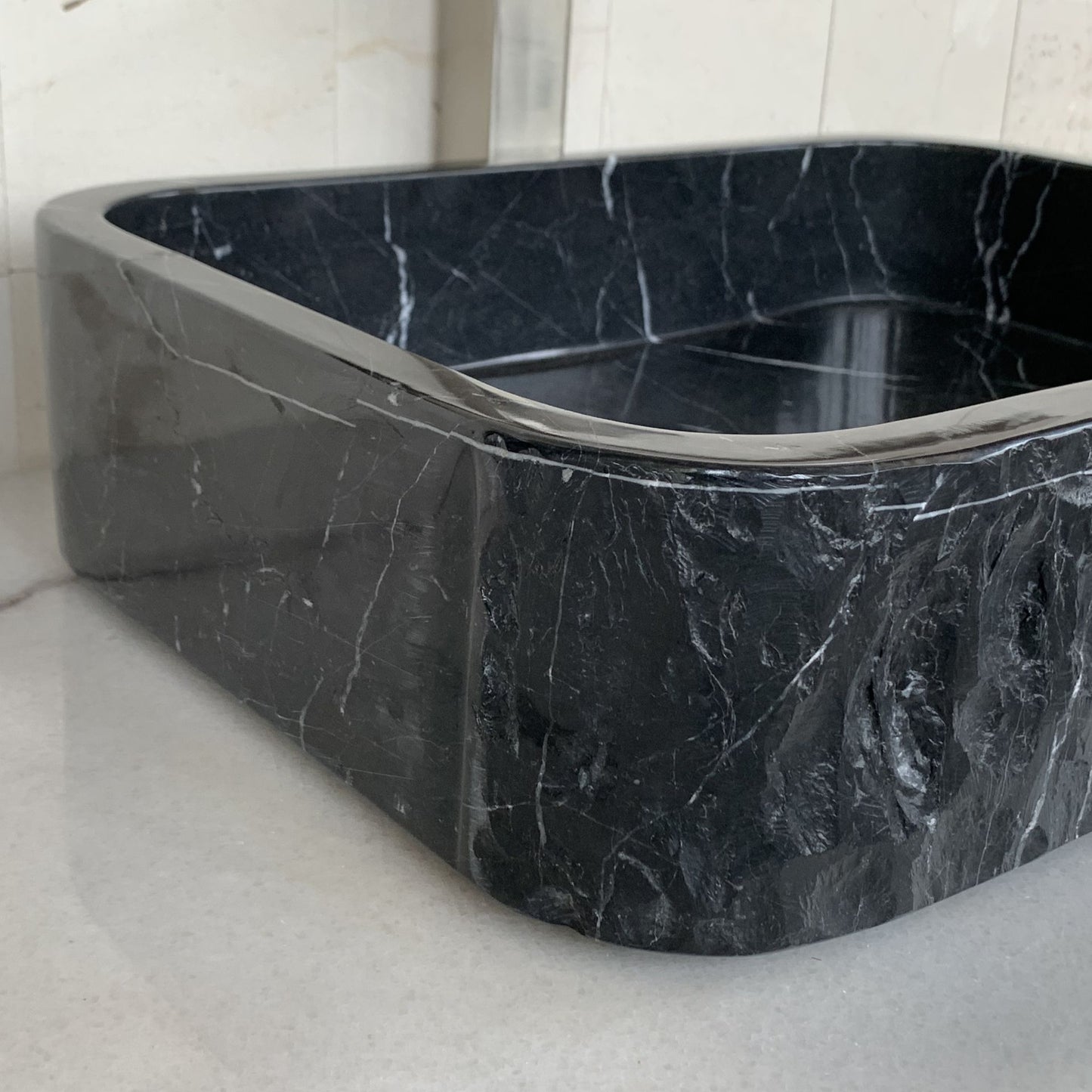 Close-up of handcrafted black marble rectangle vessel sink showing rounded corner construction, polished interior edge, natural white marble veining, and premium natural stone craftsmanship for luxury bathroom vanity design.