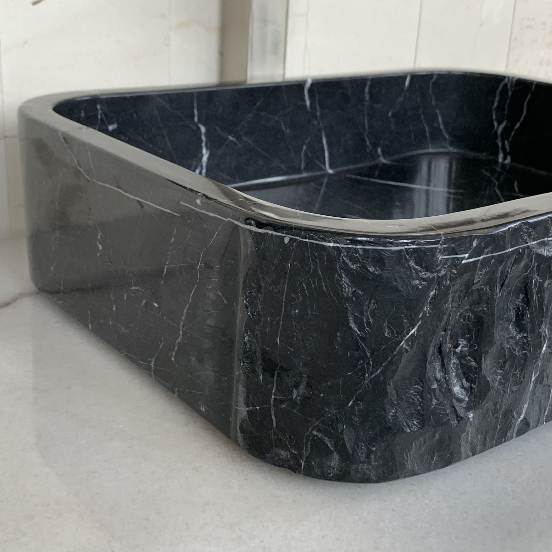 Close-up of handcrafted black marble rectangle vessel sink showing rounded corner construction, polished interior edge, natural white marble veining, and premium natural stone craftsmanship for luxury bathroom vanity design.