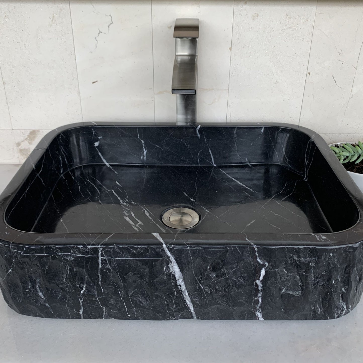 Front angle view of handcrafted black marble rectangle vessel sink featuring polished interior basin, chiseled natural stone exterior, natural white marble veining, and modern luxury bathroom vanity design.