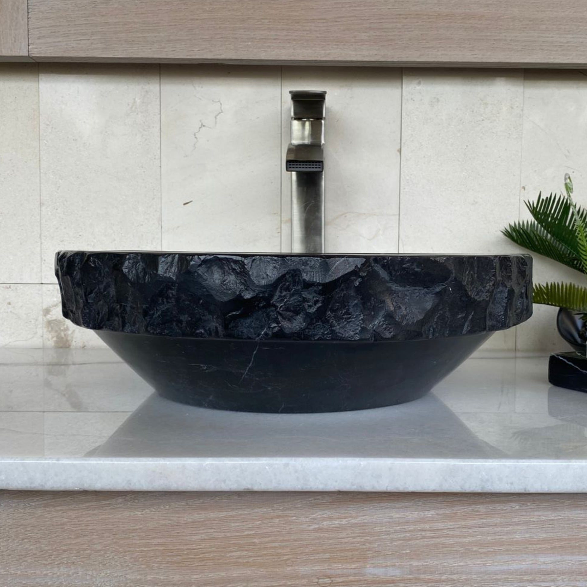 Handcrafted black marble round vessel sink with polished interior, sculpted chiseled exterior, and natural white veining displayed on a modern bathroom vanity countertop.