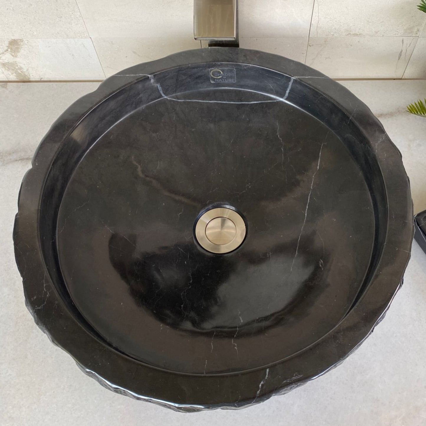 Top view of handcrafted black marble round vessel sink featuring polished interior, natural marble veining, sculpted stone edge, and standard center drain for luxury bathroom vanity installation.