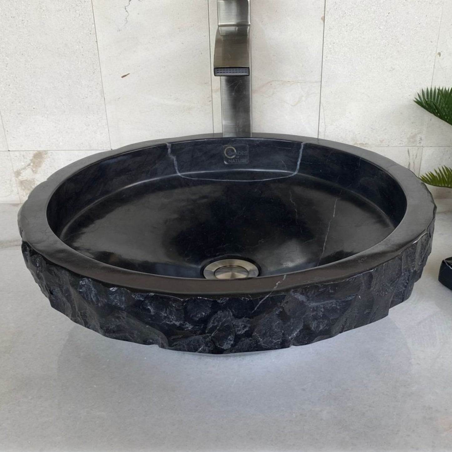 Front angle view of handcrafted black marble round vessel sink featuring polished interior basin, sculpted chiseled natural stone exterior, and modern above-counter bathroom vanity design.