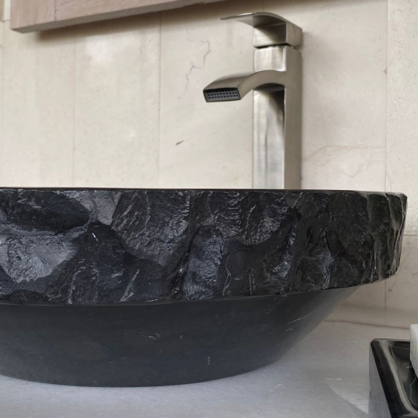 Close-up detail of handcrafted black marble round vessel sink showing sculpted chiseled natural stone exterior texture, polished marble construction, and luxury bathroom craftsmanship.