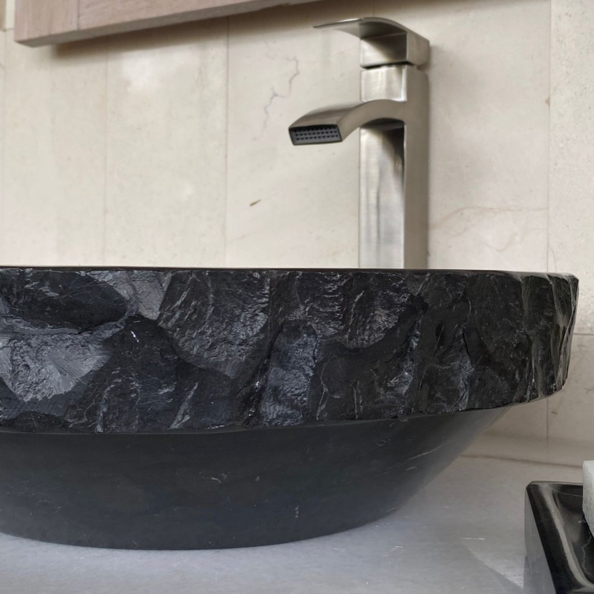 Close-up detail of handcrafted black marble round vessel sink showing sculpted chiseled natural stone exterior texture, polished marble construction, and luxury bathroom craftsmanship.