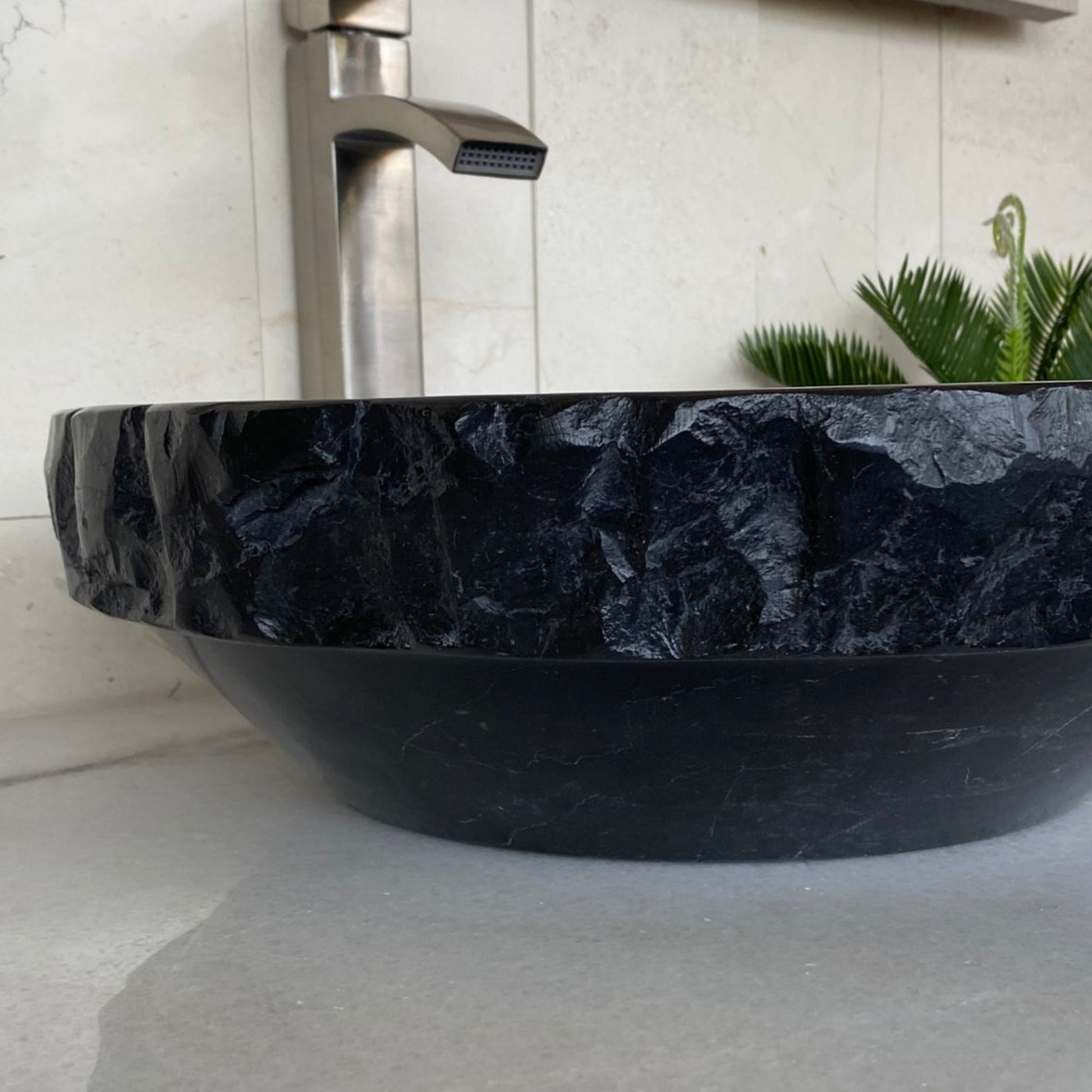 Side angle view of handcrafted black marble round vessel sink featuring sculpted chiseled natural stone exterior, polished marble construction, and modern luxury bathroom vanity styling.