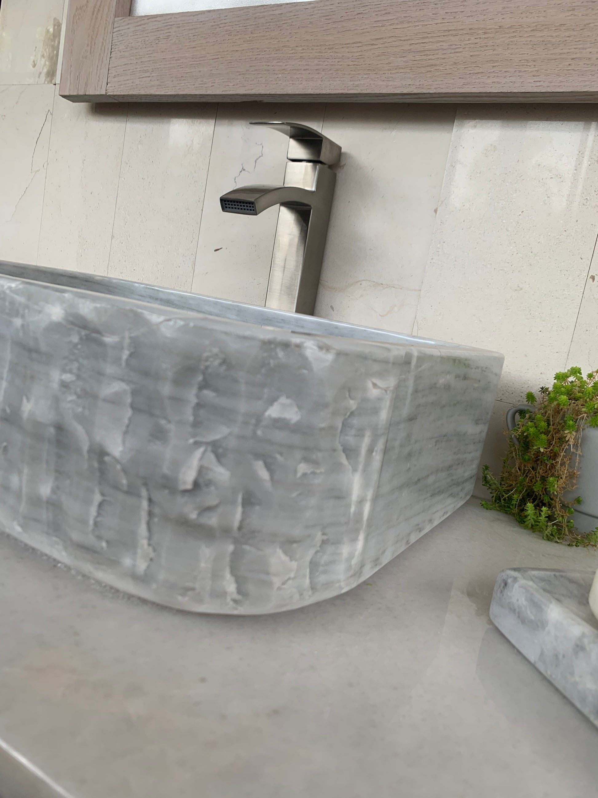 Side-angle view of a rectangular chiseled light gray marble vessel sink, showcasing how the hand-carved stone texture on the front corner smoothly transitions into a polished side wall.