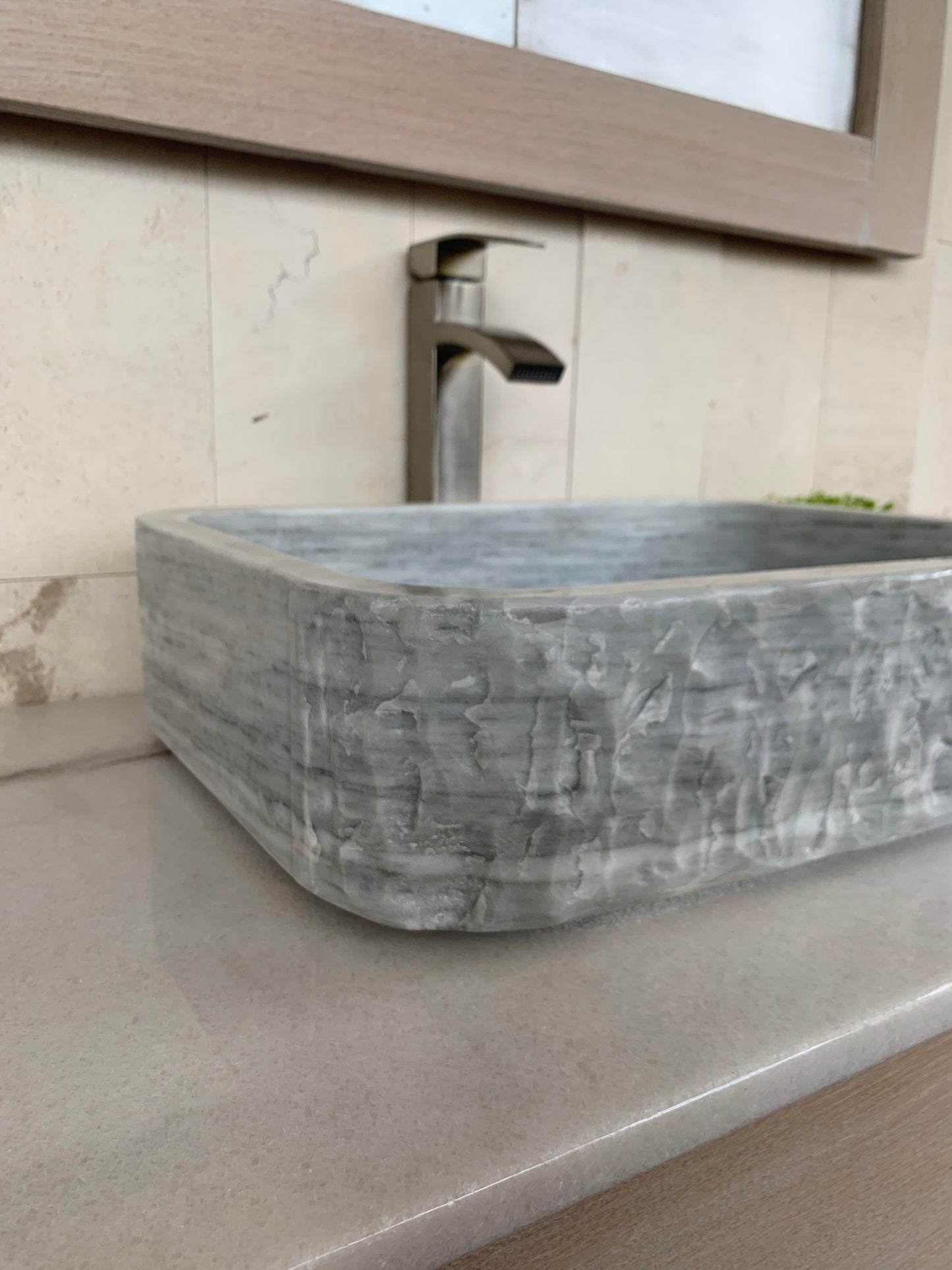 Angled side view of a rectangular natural stone bathroom basin made of gray marble, highlighting its rustic chiseled exterior front, and smooth polished sides