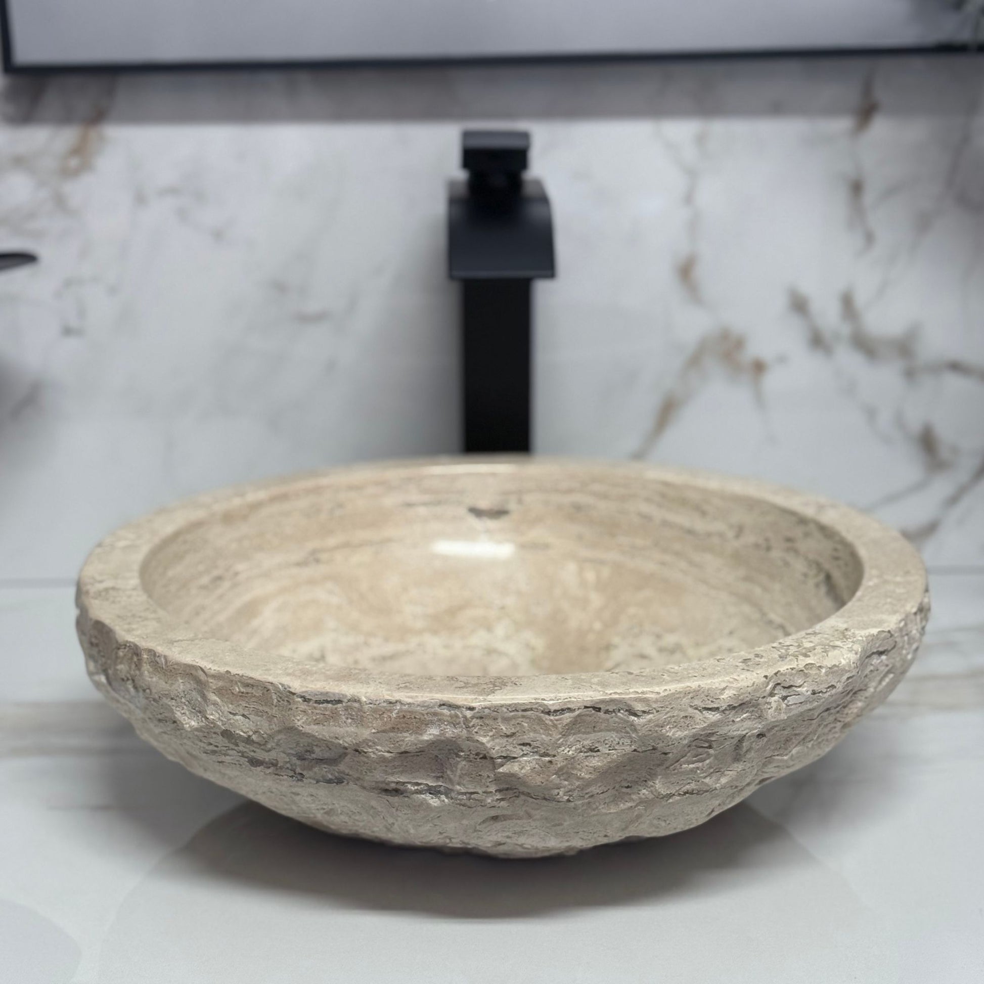 High-angle view looking into a round beige travertine vessel sink, showcasing the smooth polished interior with unique natural stone veining and a rugged chiseled exterior.