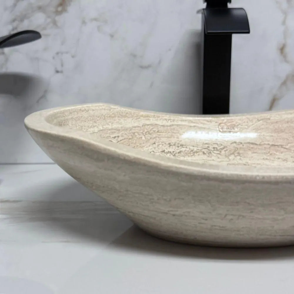 Close-up profile view of an oval polished tan travertine vessel sink, highlighting the completely smooth exterior finish and the elegant natural stone veining along its curved modern look.