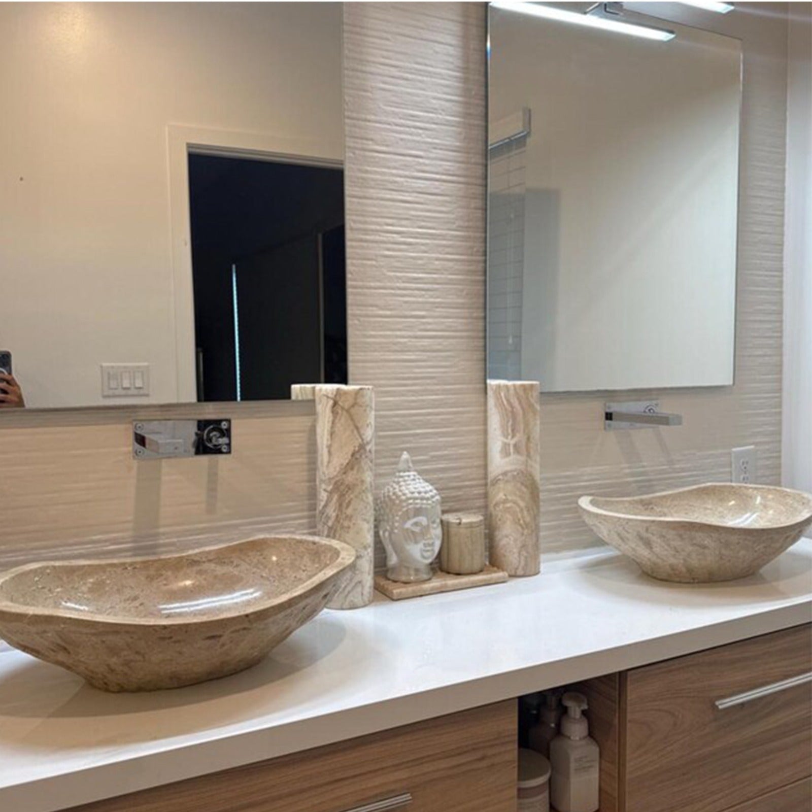 A pair of natural stone bathroom basins made of beige travertine, highlighting the rustic chiseled exterior surfaces and polished inner bowls arranged in a modern dual vanity bathroom setting.