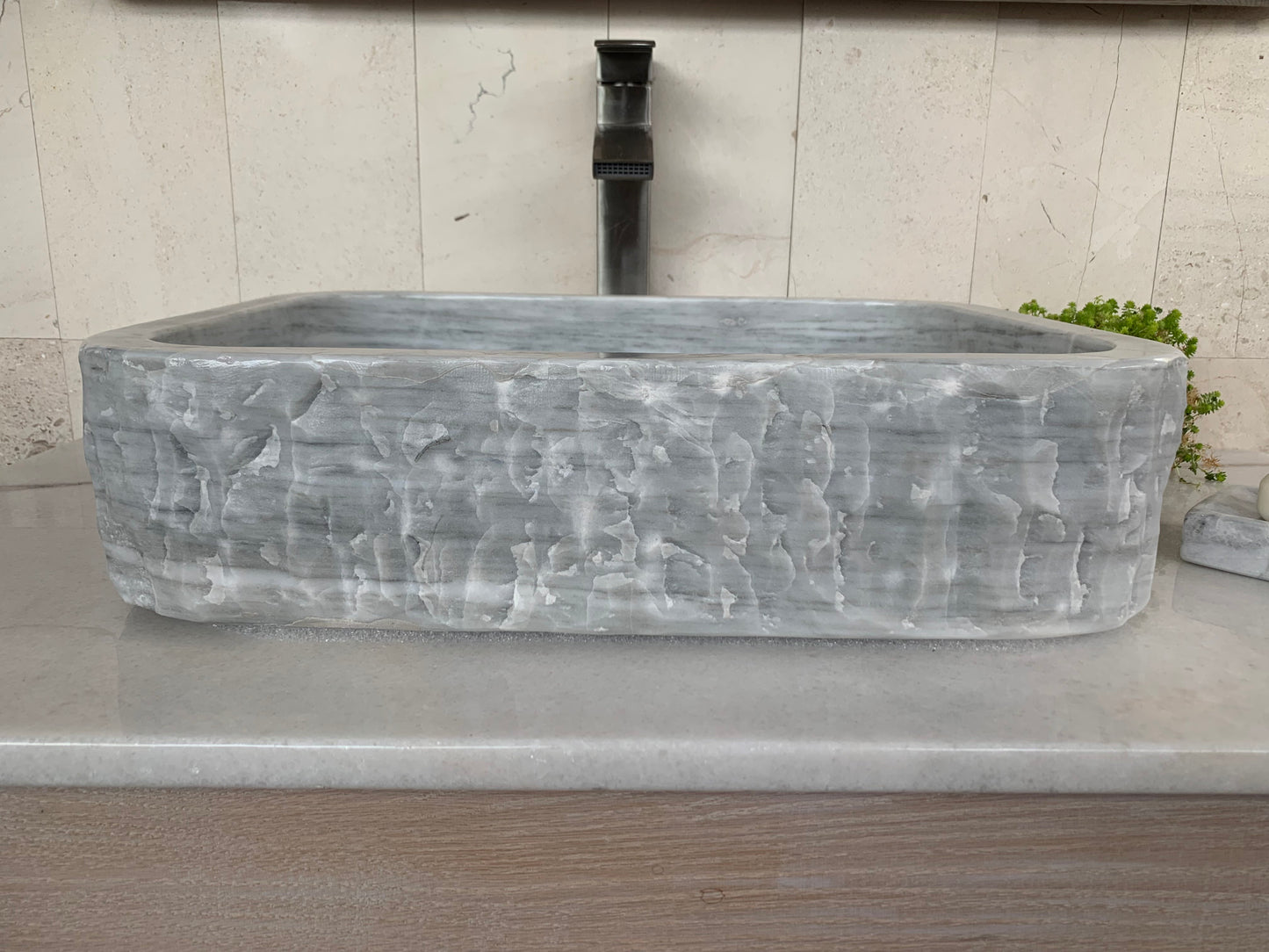 Front view of a rectangular light gray marble vessel sink with a rustic chiseled exterior finish and clean profile.