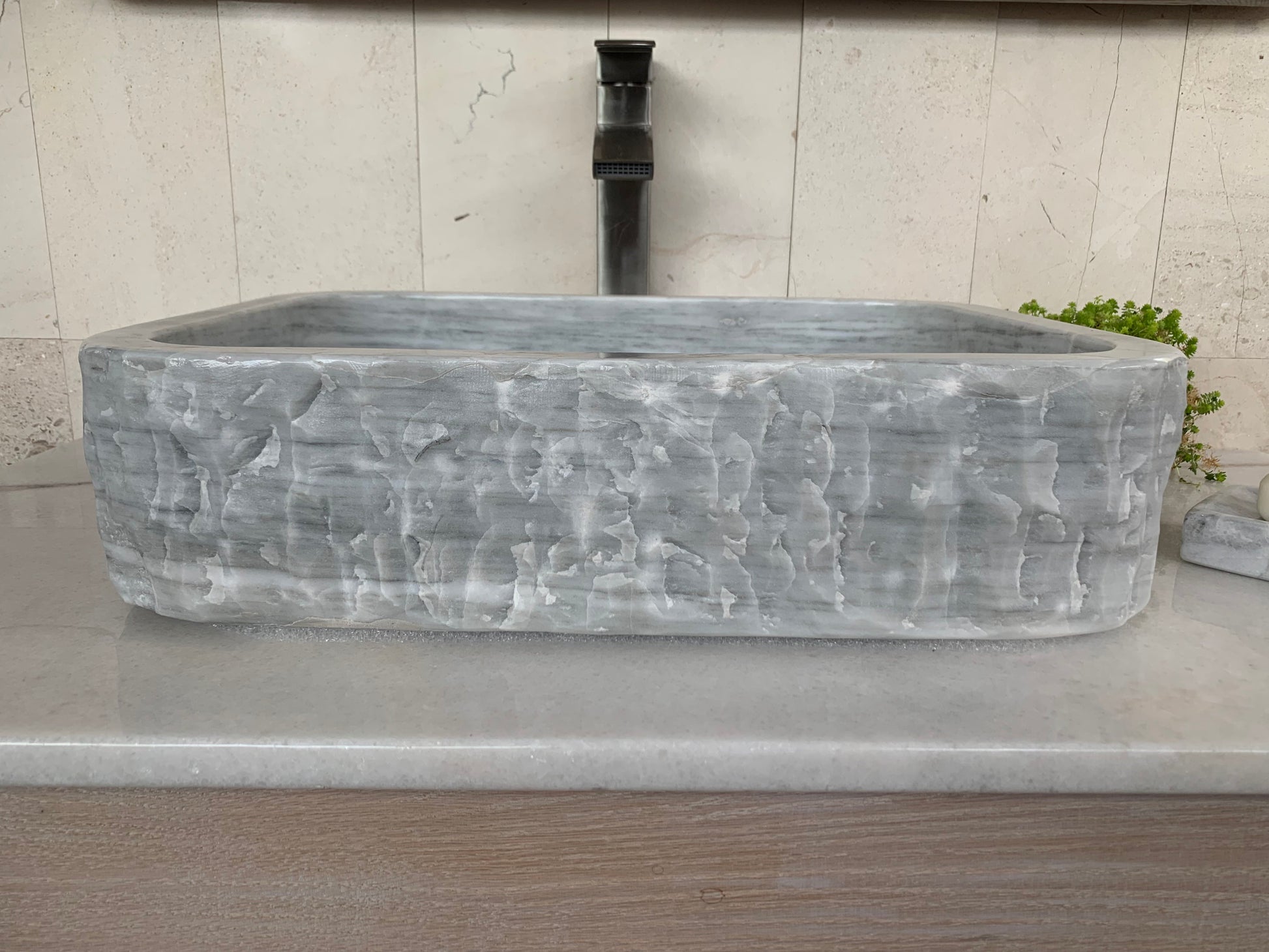 Front view of a rectangular light gray marble vessel sink with a rustic chiseled exterior finish and clean profile.