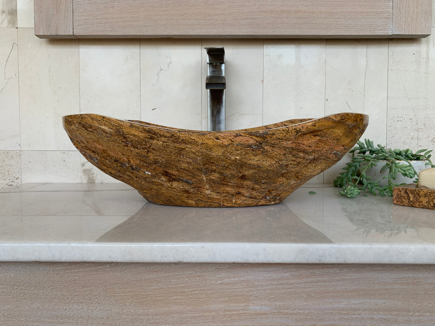 Handcrafted oval red travertine vessel sink on a bathroom countertop with a modern faucet and natural stone accessory.