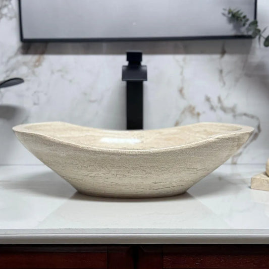 Curved oval bathroom wash basin made of polished beige travertine, showcasing a completely smooth exterior and elegant organic patterns, displayed in a contemporary vanity setting.