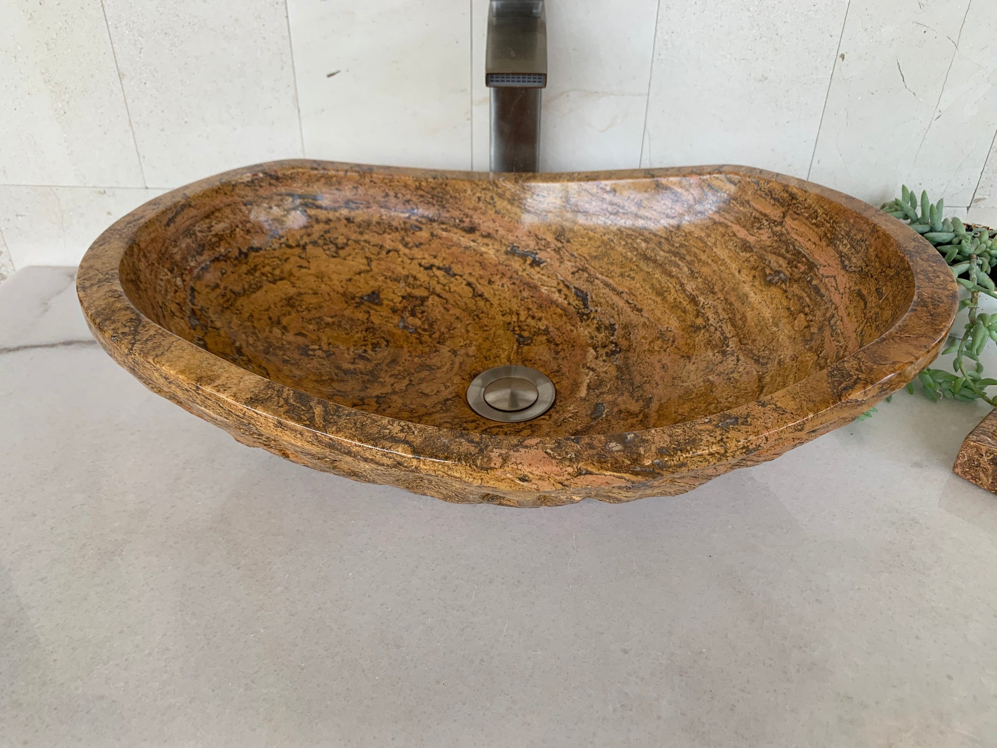 Handcrafted oval red travertine vessel sink with polished interior and natural textured stone edge on a bathroom countertop.