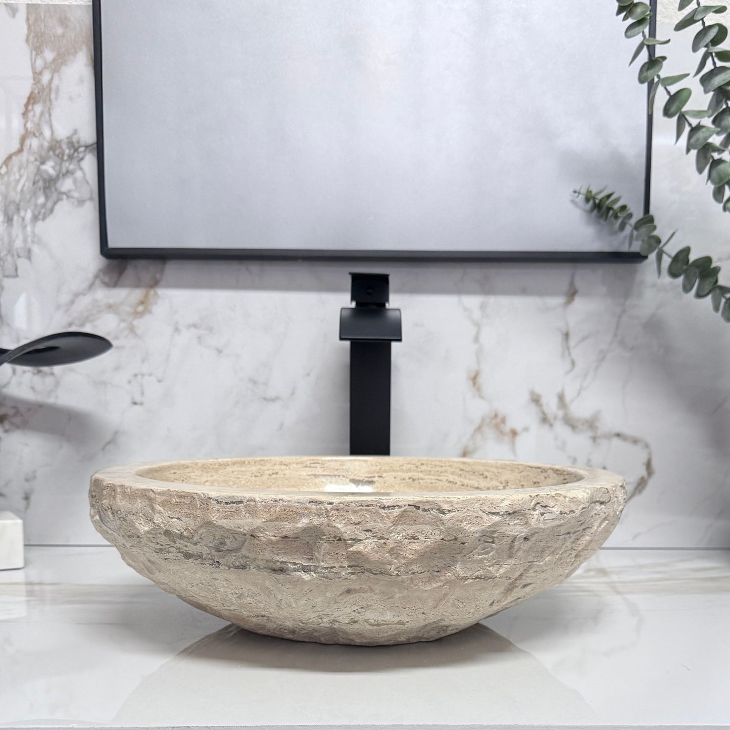 Beige travertine vessel sink with a hand-carved chiseled finish and a matching natural stone soap tray, displayed in a contemporary bathroom setting.