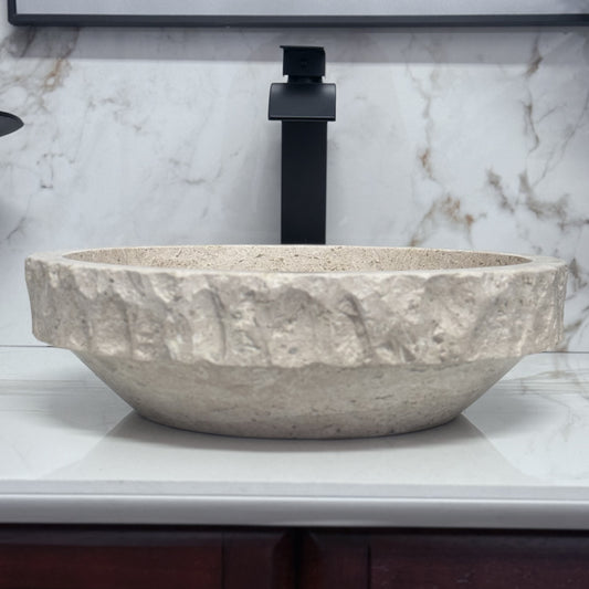 Round tan travertine vessel sink with chiseled rim for natural stone bathroom vanity.