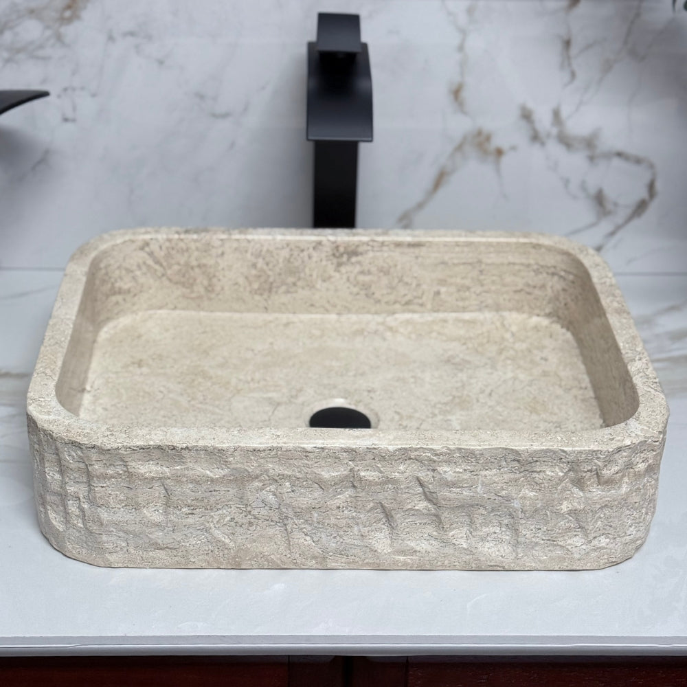 High-angle overhead view looking into a rectangular chiseled tan travertine vessel sink, highlighting the smooth polished interior, unique natural stone grain, and thick rugged rustic edge.